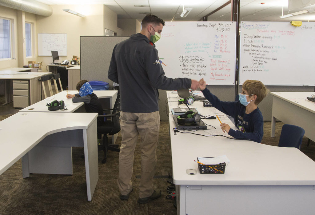 Tom Van Acker gives his son, Mason, a fist bump as he heads to work in another part the building after dropping off his sons at a classroom set up at Electroimpact in Mukilteo. Declan, his other son, is at left. (Andy Bronson / The Herald)
