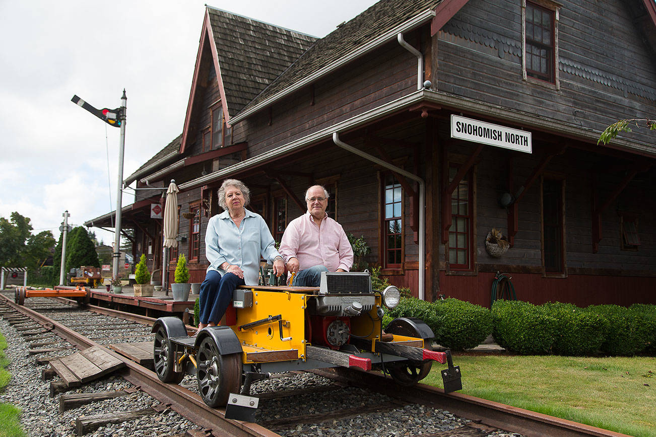 Bruce and Marie Ferguson sit on a rail car set atop train tracks in their yard at home on Tuesday, Sept. 22, 2020 in Snohomish, Washington.  The Ferguson's built in their home in 2007 to mimic a Northern Pacific train depot. (Andy Bronson / The Herald)