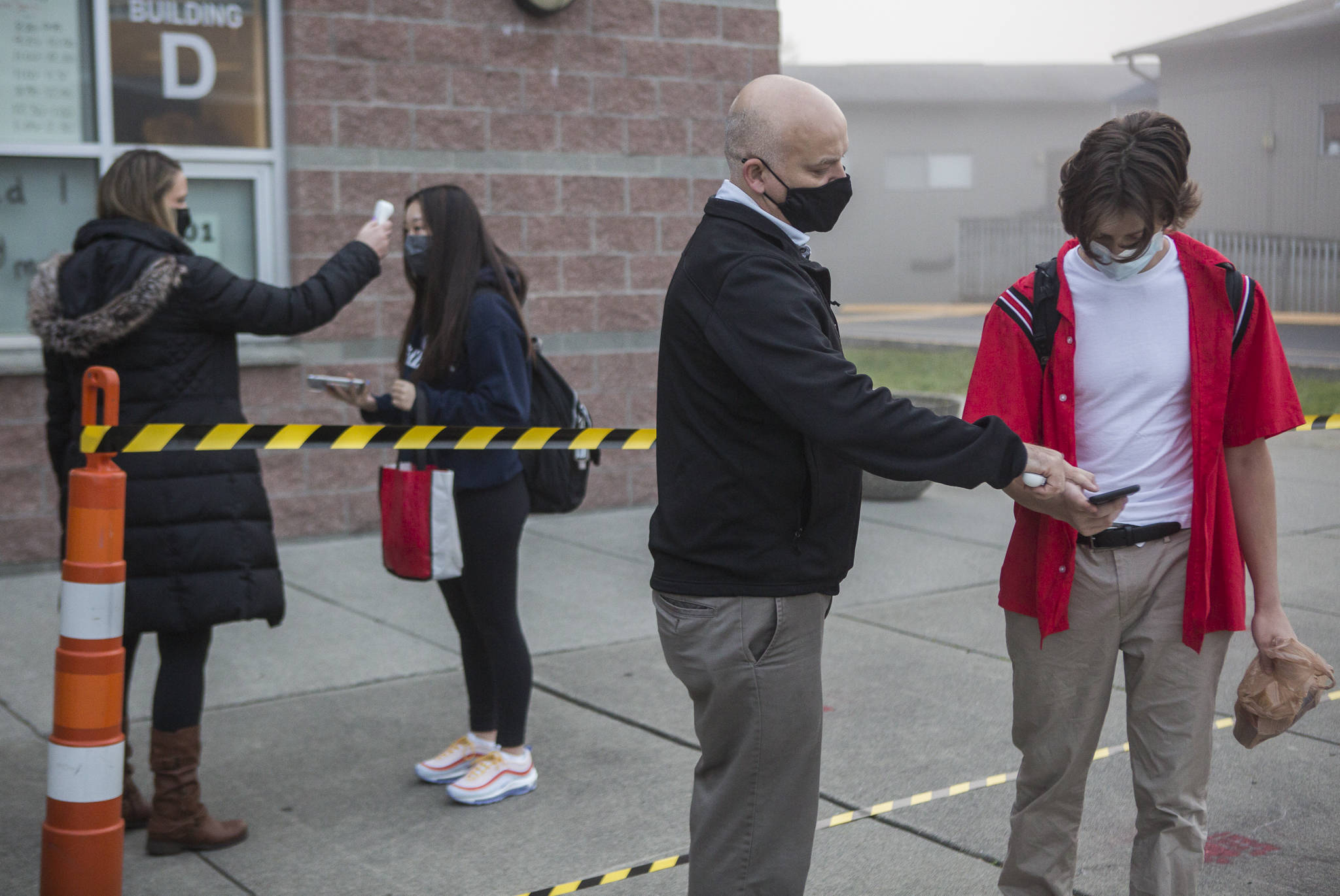 Dean of Students Jeff Latta (center) helps a student through their online health questionnaire while Athletic Director Cassie Snell (left) checks a student’s temperature before the start of class at Archbishop Murphy on Tuesday in Everett. (Olivia Vanni / The Herald)