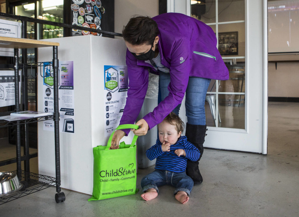 Whitney Stohr and her son Malachi Stohr-Hendrickson, 2, add diapers to a ChildStrive donation box on Oct. 7 at Crucible Brewing in Everett. Malachi receives early intervention services through ChildStrive. (Olivia Vanni / The Herald)
