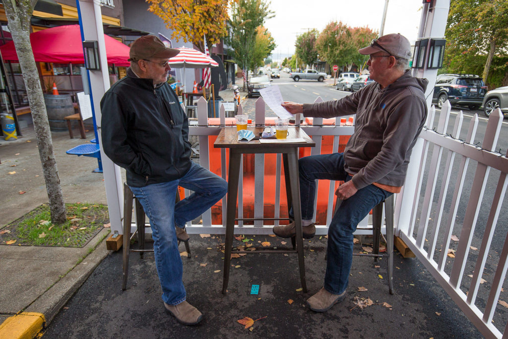 Scott McEntire and Jim Coe enjoy a drink and lunch in an outdoor seating tent at the Salish Sea Brewing Co. on Dayton Street in Edmonds on Monday. (Andy Bronson / The Herald)
