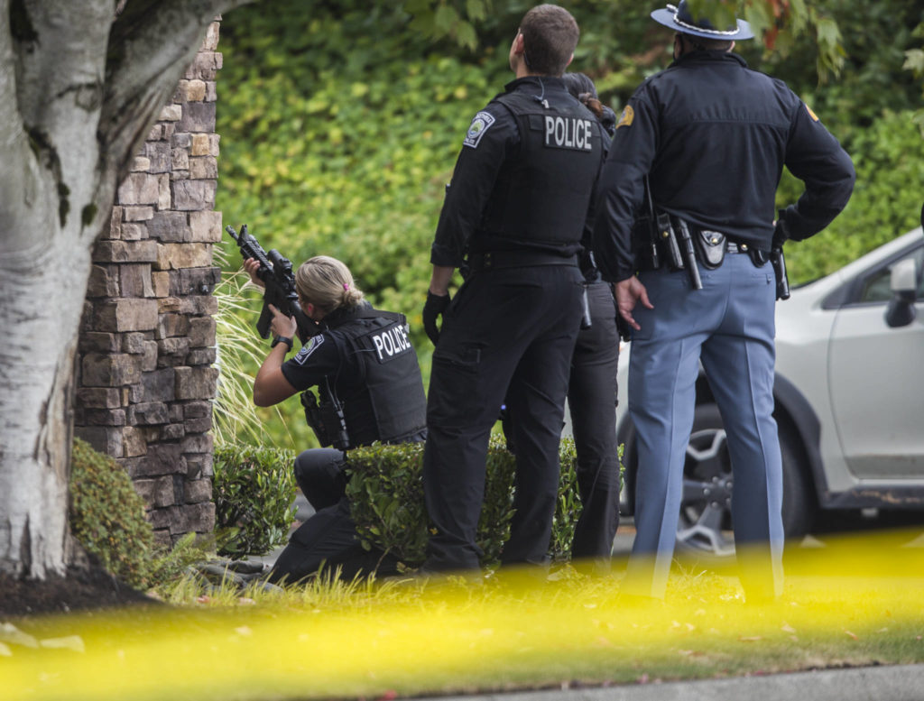 A police officer looks through a scope at a carjacking suspect on Wednesday near Mill Creek. (Olivia Vanni / The Herald) 
