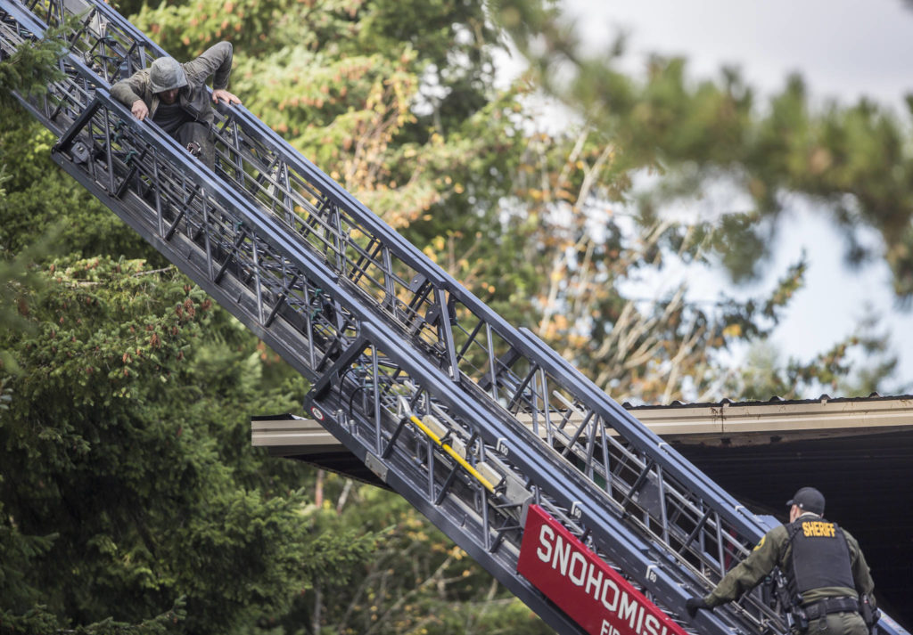 A carjacking suspect slowly makes his way down a fire truck ladder as a sheriff’s deputy waits on Wednesday near Mill Creek. (Olivia Vanni / The Herald)
