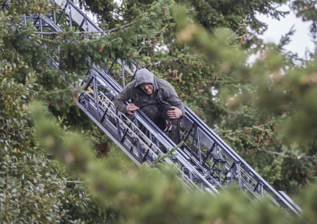 A carjacking suspect grabs his left leg and grimaces due to an apparent wound as he climbs down a ladder on Wednesday near Mill Creek. (Olivia Vanni / The Herald) 
