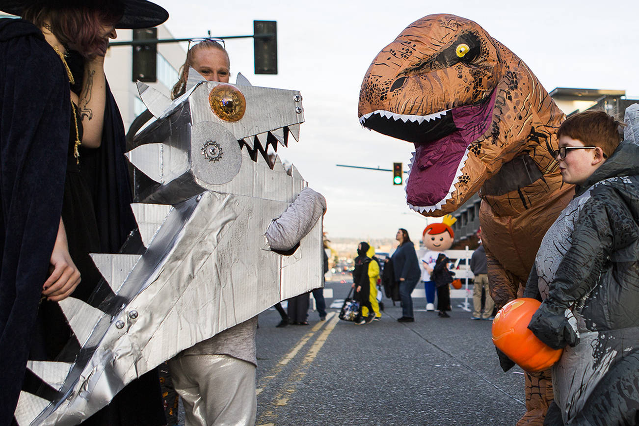 People in dinosaur costumes greet each other during Downtown Trick-or-Treating on Oct. 31, 2019 in Everett, Wash. Health officials have discouraged trick-or-treating this year. (Olivia Vanni / The Herald)