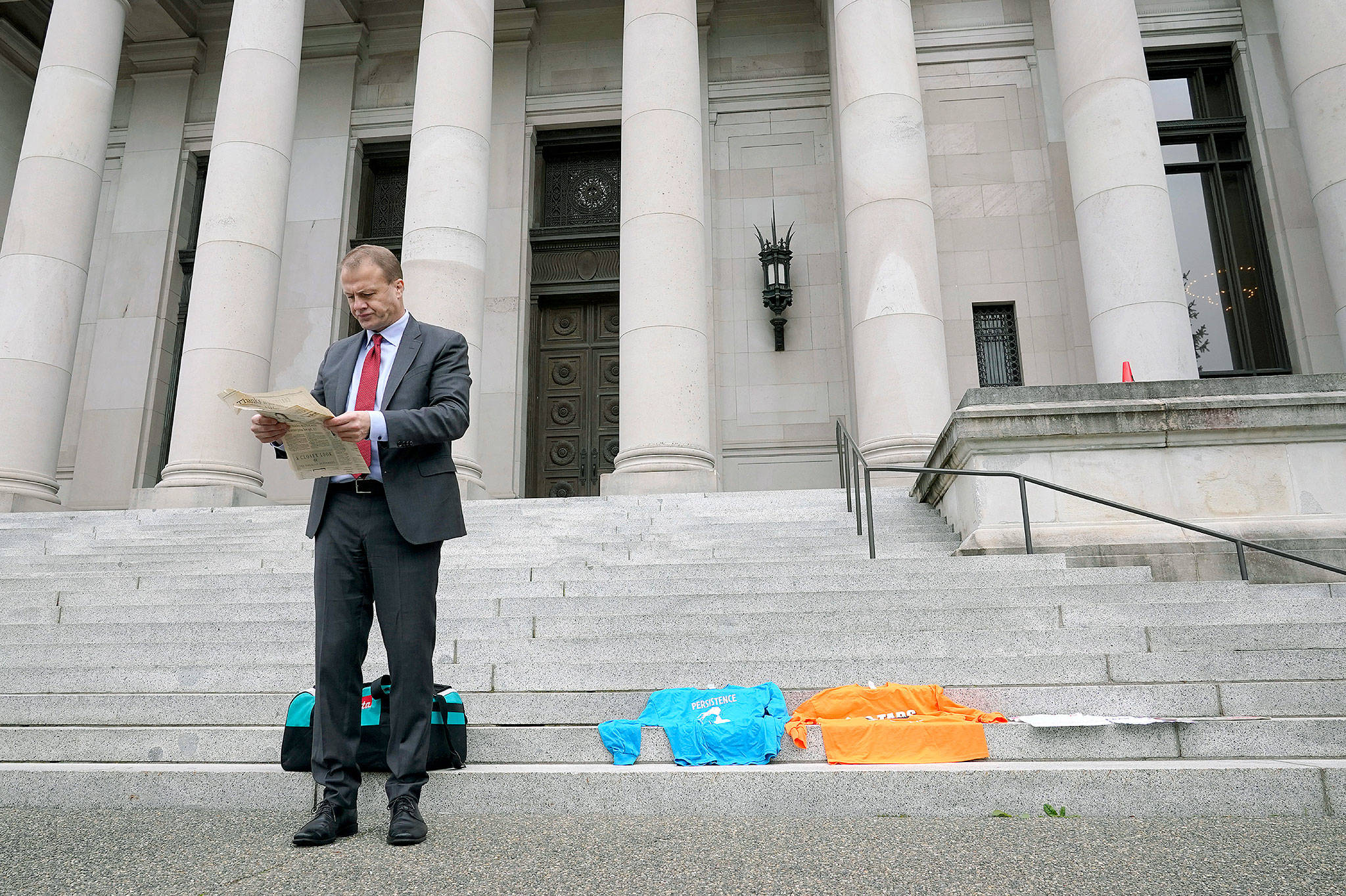 Initiative promoter Tim Eyman reads a newspaper article from the year 2000 about his long-running campaign for $30 car tabs as he waits to talk to reporters Thursday in front of the Temple of Justice at the Capitol in Olympia. (AP Photo/Ted S. Warren)