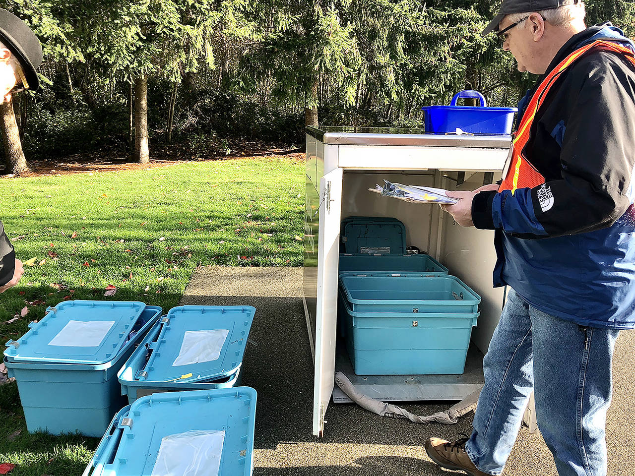 Two Snohomish County Auditor’s Office workers removed the filled blue plastic tubs inside a drop box in front of the Mukilteo Library on Election Day 2018 and placed empty tubs inside to catch the next round of ballots. (Andrea Brown / Herald file)