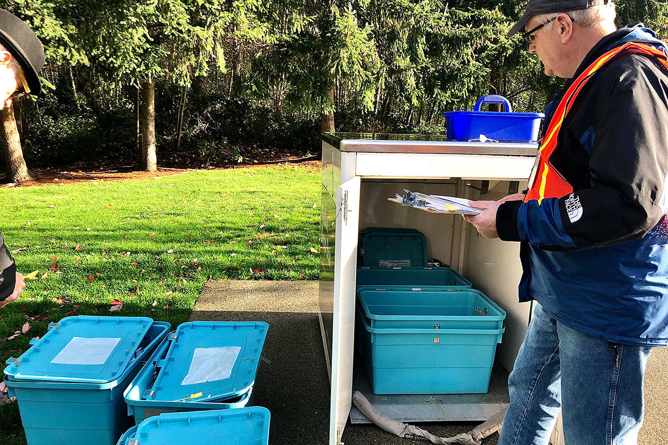 Two Snohomish County Auditor's Office workers removed the filled blue plastic tubs inside a drop box in front of the Mukilteo Library on Election Day 2018 and placed empty tubs inside to catch the next round of ballots. (Andrea Brown / Herald file)