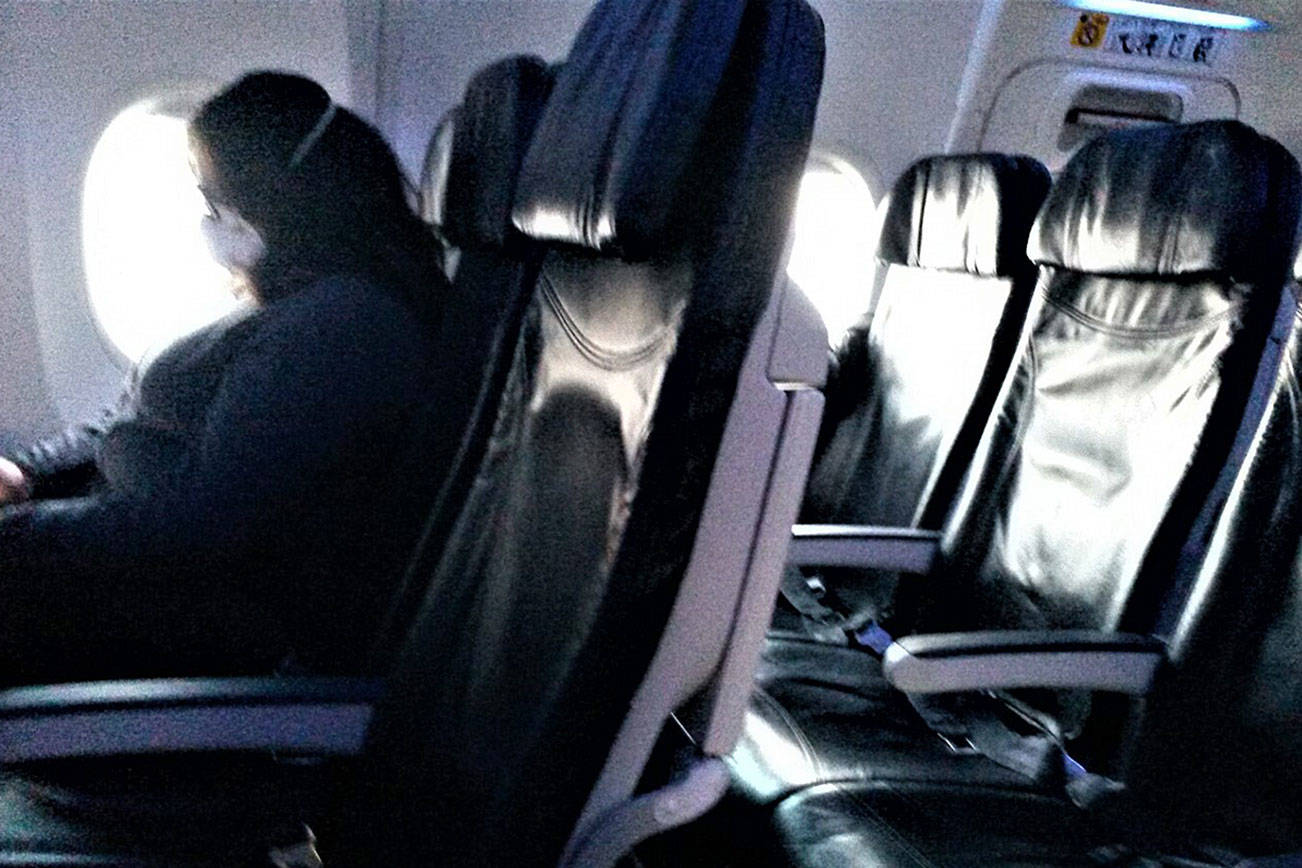 A masked passenger sits in front of an empty row of seats on an Alaska Airlines flight from Spokane to Sea-Tac Monday evening. (Julie Muhlstein) 20201026