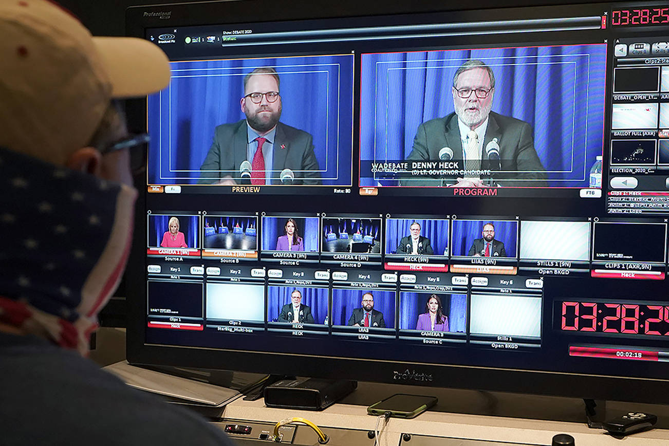 A technician works in a TVW control room, Thursday, Oct. 22, 2020, during a debate in Olympia, Wash., between U.S. Rep. Denny Heck, D-Wash., shown at right on the video monitor, and Washington Sen. Marko Liias, D-Lynnwood, left, in the race for lieutenant governor of Washington state. (AP Photo/Ted S. Warren)
