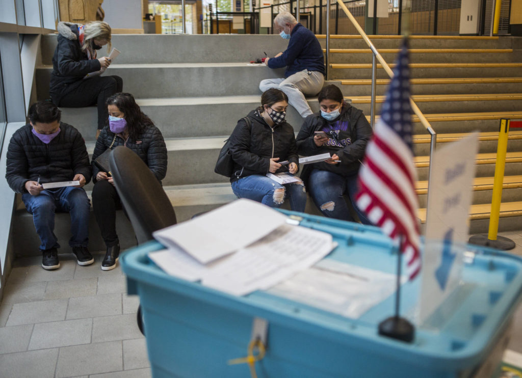 People sit outside of the County Public Meeting Room to fill out and turn in their ballots on Tuesday in Everett. (Olivia Vanni / The Herald) 
