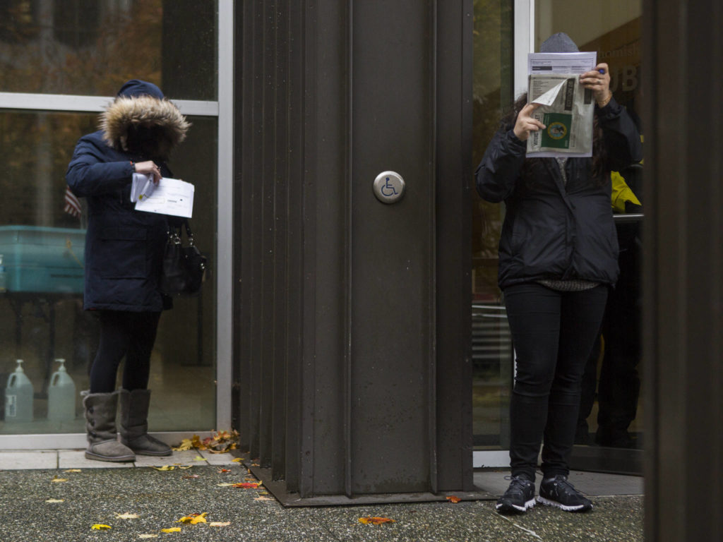 People stand outside in the rain and fill out their ballots on Tuesday in Everett. (Olivia Vanni / The Herald) 
