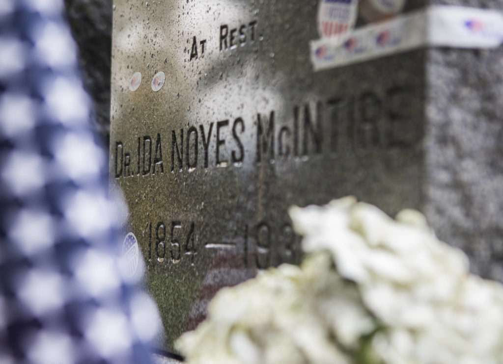 The gravestone of suffragist Dr. Ida Noyes McIntire, surrounded by flowers and covered in “I voted” stickers, at the Evergreen Cemetery on Wednesday in Everett. (Olivia Vanni / The Herald) 

