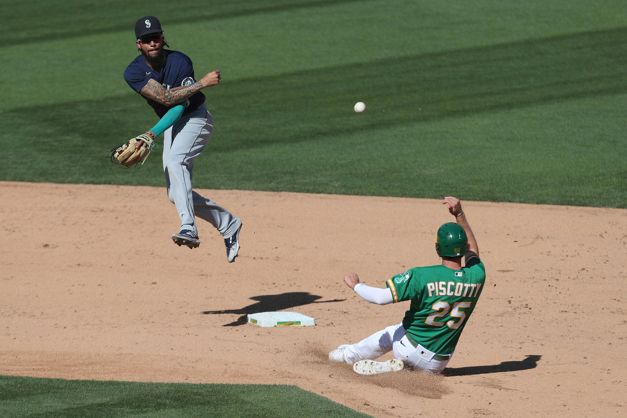 The Mariners’ J.P. Crawford (left) throws to first base as the Athletics’ Stephen Piscotty slides into second on a double play during the seventh inning of a game on Sept. 26, 2020, in Oakland, Calif. (AP Photo/Jed Jacobsohn)