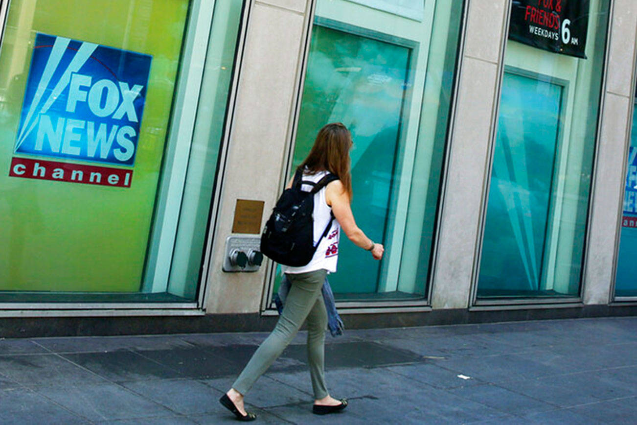 FILE- People pass the News Corporation headquarters building and Fox News studios in New York on Aug. 1, 2017. Several Fox News Channel executives and on-air personalities were exposed last week to a person on a private plane who later tested positive for COVID-19. It has led to some restrictions at the network. Anchor Bret Baier said Monday that he's tested negative three times in the wake of the flight and will be doing his nightly news show from home this week. (AP Photo/Richard Drew, File)