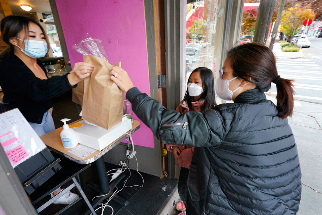 Customer Kyung Kim (right) and her daughter Alexa Oh, 9, are handed their purchased baked goods through an open door by cashier Donna Te as they maintain social distance and wear masks, Thursday in Seattle. Washington state and county health officials have warned of a spike in coronavirus cases across the state, and pleaded with the public to take the pandemic more seriously heading into the winter holidays. (Elaine Thompson / Associated Press)