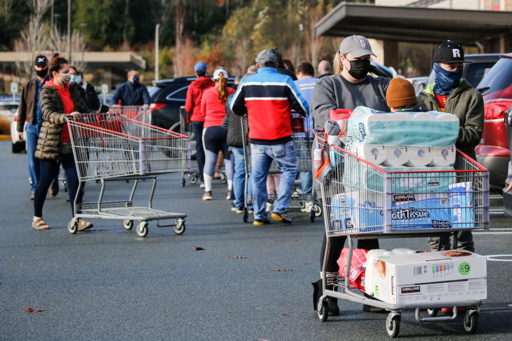 A Costso customer pushes his cart of groceries past others waiting to get in the store Sunday morning in Lynnwood. (Kevin Clark / The Herald)
