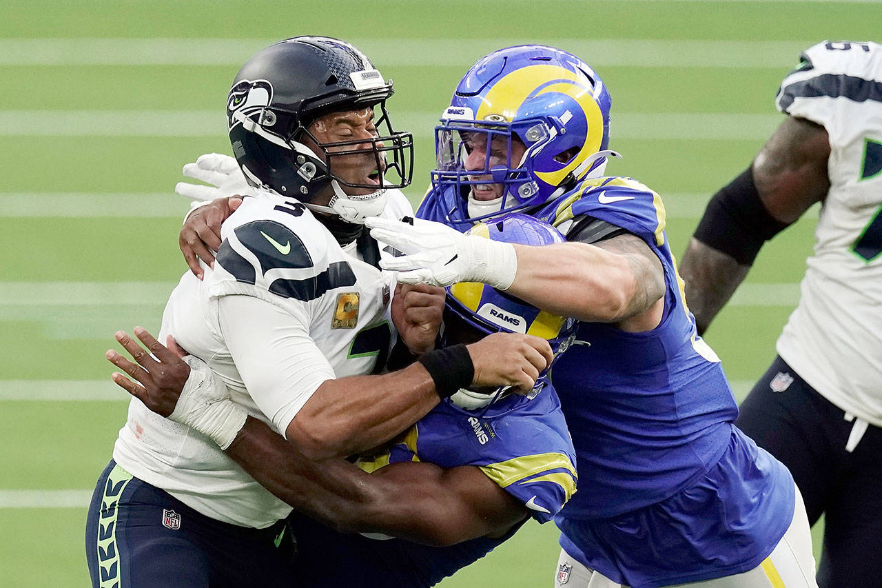 Seattle Seahawks quarterback Russell Wilson (3) is tackled by two Los Angeles Rams defenders Sunday. (Associated Press)