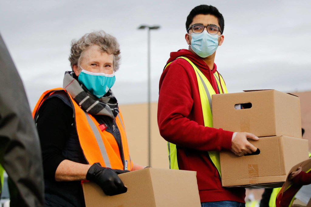Mary Bickmell (left) and Shivam Vahadari carry boxes for loading Friday during a drive-thru food distribution at Everett Mall. (Kevin Clark / The Herald)
