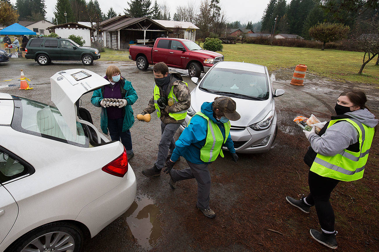 Volunteers load a car with food during a drive-through event for families in need called the “Colors of Fall” at the Darrington Food Bank on Monday, Nov. 23, 2020 in Darrington, Washington. Stops along the drive-thru provided hand sanitizer, masks, food boxes, assistance information for those that need help with early learning, utilities, mental health, etc.  (Andy Bronson / The Herald)