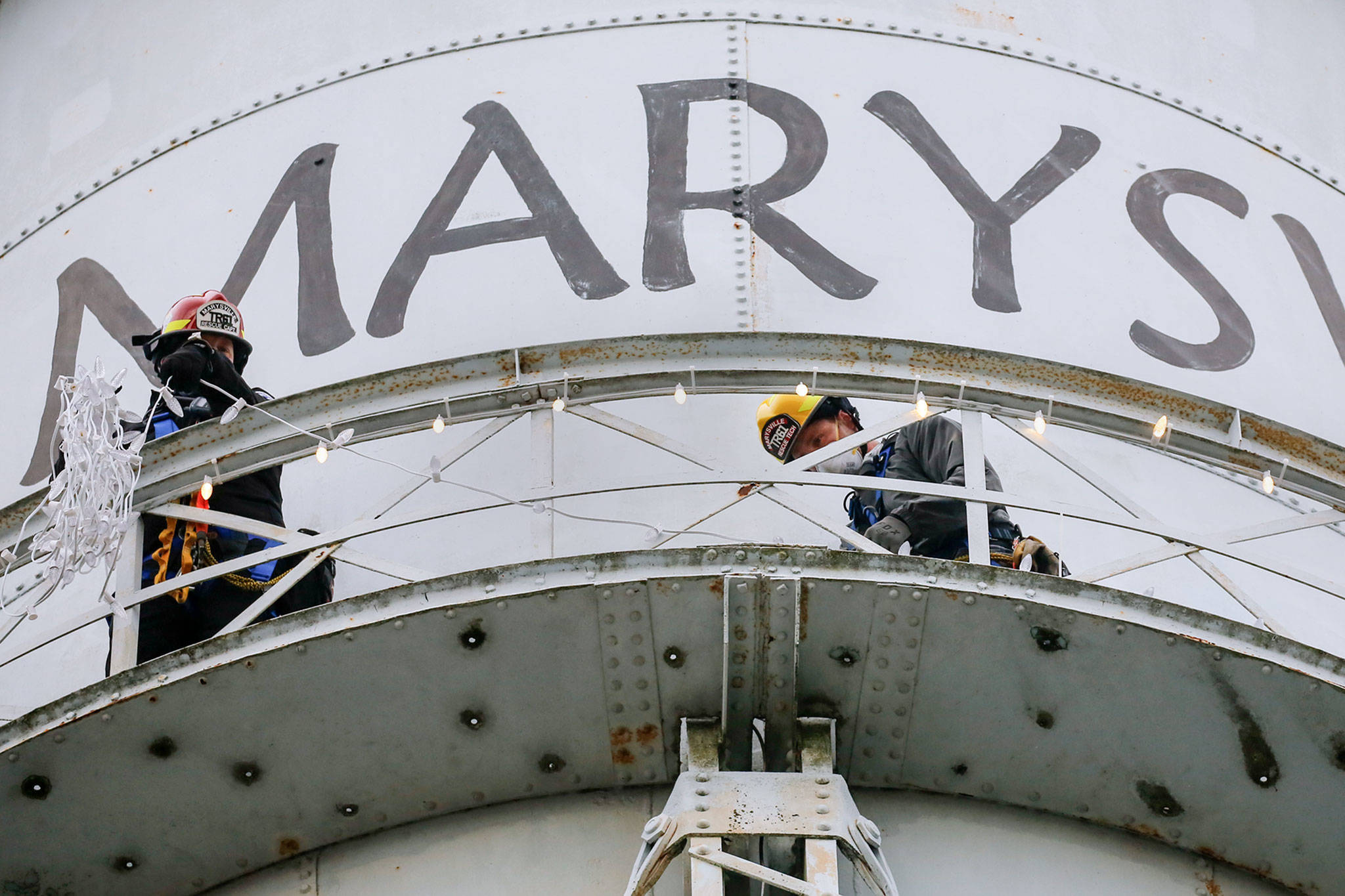 Marysville rescue team members Matt Campbell (left) and Tobin McGowan string lights on the Marysville water tower Friday. Holiday lights have been a tradition for decades, but last year the city skipped the decoration because the tower needed repairs. (Kevin Clark / The Herald)