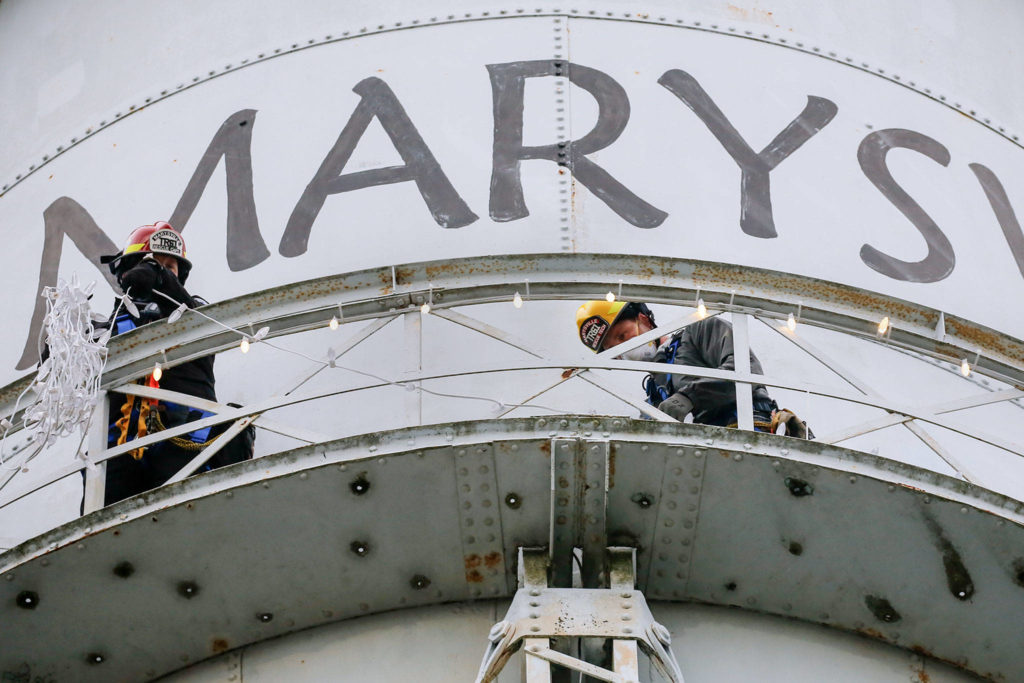 Marysville rescue team members Matt Campbell (left) and Tobin McGowan string lights on the Marysville water tower Friday. Holiday lights have been a tradition for decades, but last year the city skipped the decoration because the tower needed repairs. (Kevin Clark / The Herald)
