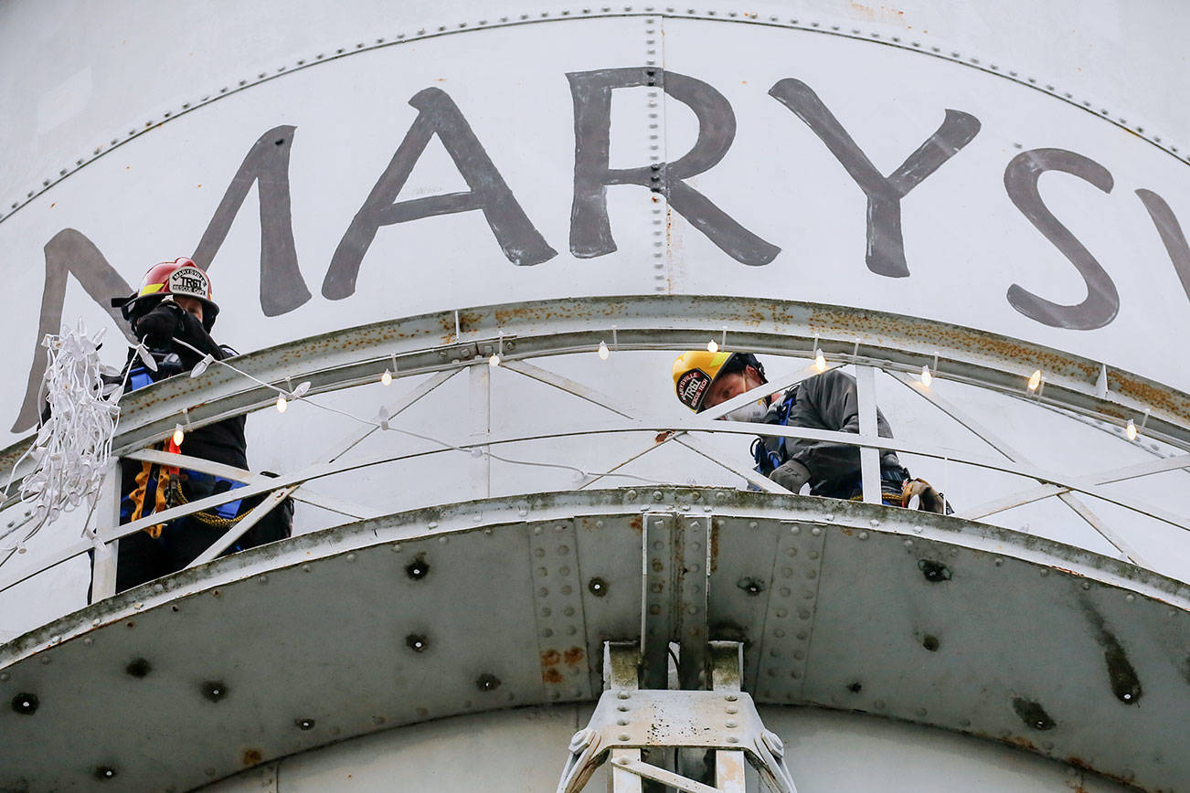 Members of the Marysville resue team, Matt Campbell (left) and Tobin McGowan string lights on the Marysville water towner Friday November 20, 2020. Holiday lights have been a tradition for decades, but last year the city skipped it because the tower needed repairs. (Kevin Clark / The Herald)