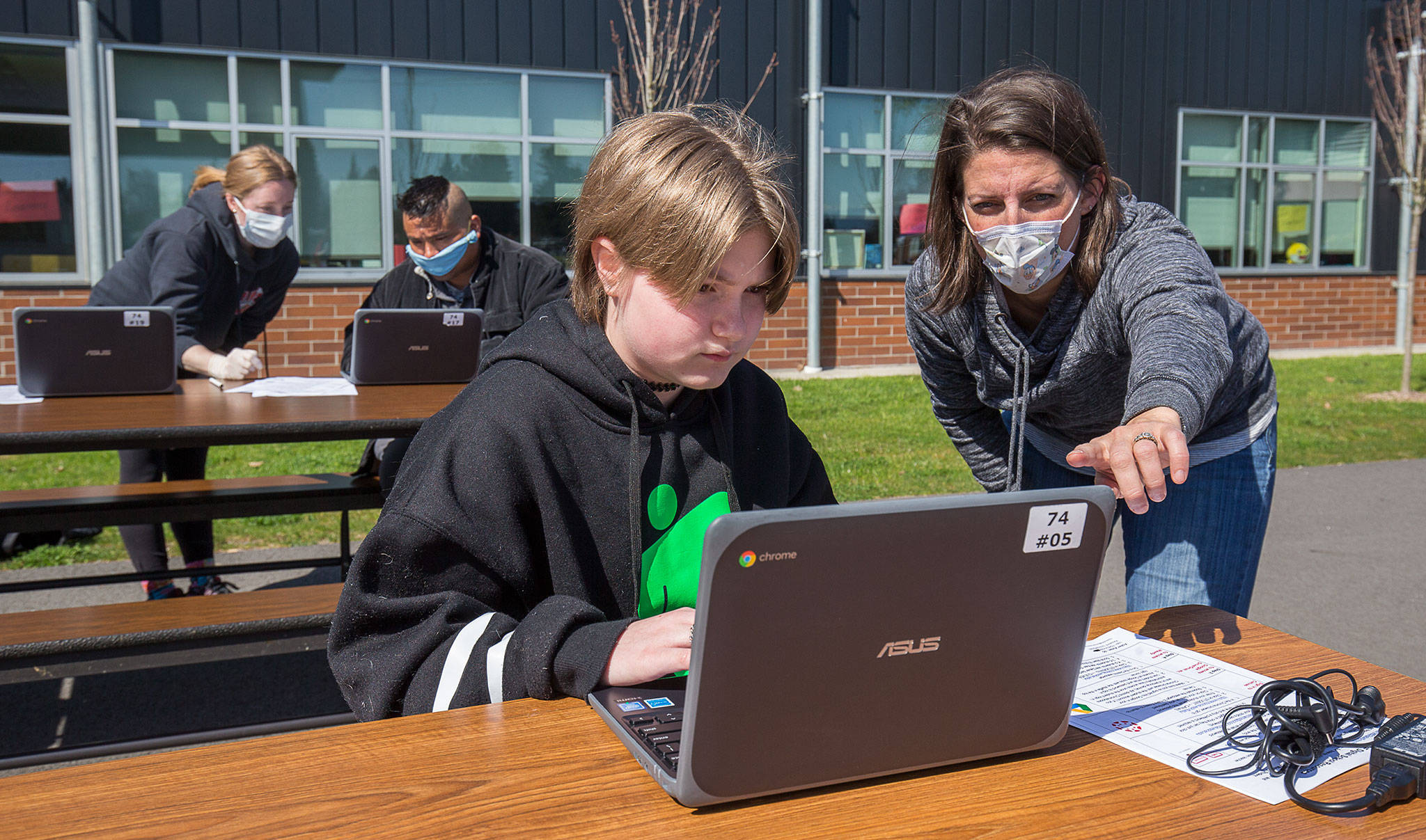 Fifth-grader Vivian Fisher get help setting up a laptop from Jody Urban at Frank Wagoner Elementary in April, as the Monroe School District began preparations for students to finish the school year remotely. (Andy Bronson / Herald file photo)