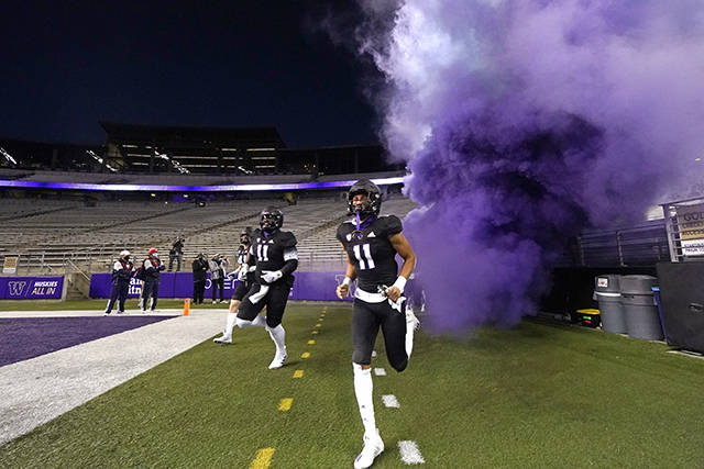 Washington players run from a purple cloud onto the field before a game against Arizona, in a stadium empty of spectators Saturday in Seattle. (AP Photo/Elaine Thompson)