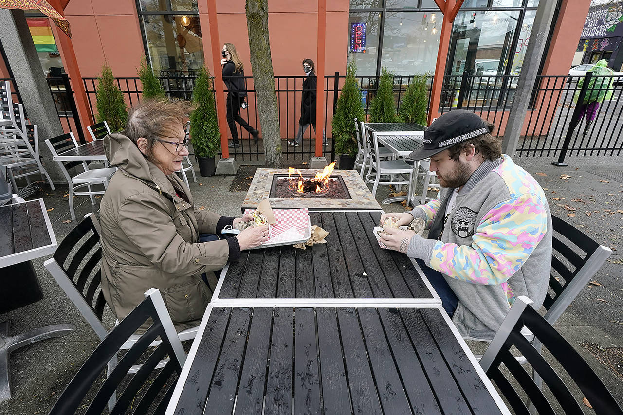 Diners Bonnie Breitman (left) and Casey McGan huddle near an outdoor gas fire as they eat lunch outside in a blustery wind Nov. 17 in Bellingham. (AP Photo/Elaine Thompson)