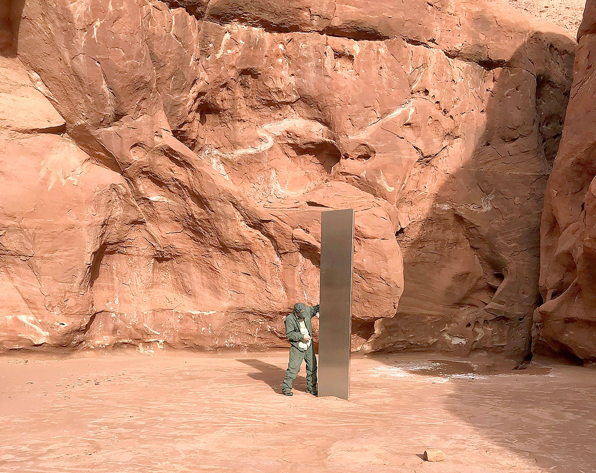 A Utah state worker stands next to a metal monolith in the ground in a remote area of red rock Nov. 18 in Utah. The mysterious silver monolith found in the Utah desert has disappeared less than 10 days after it was spotted by wildlife biologists performing a helicopter survey of bighorn sheep, federal officials and witnesses said. (Utah Department of Public Safety via AP, File)