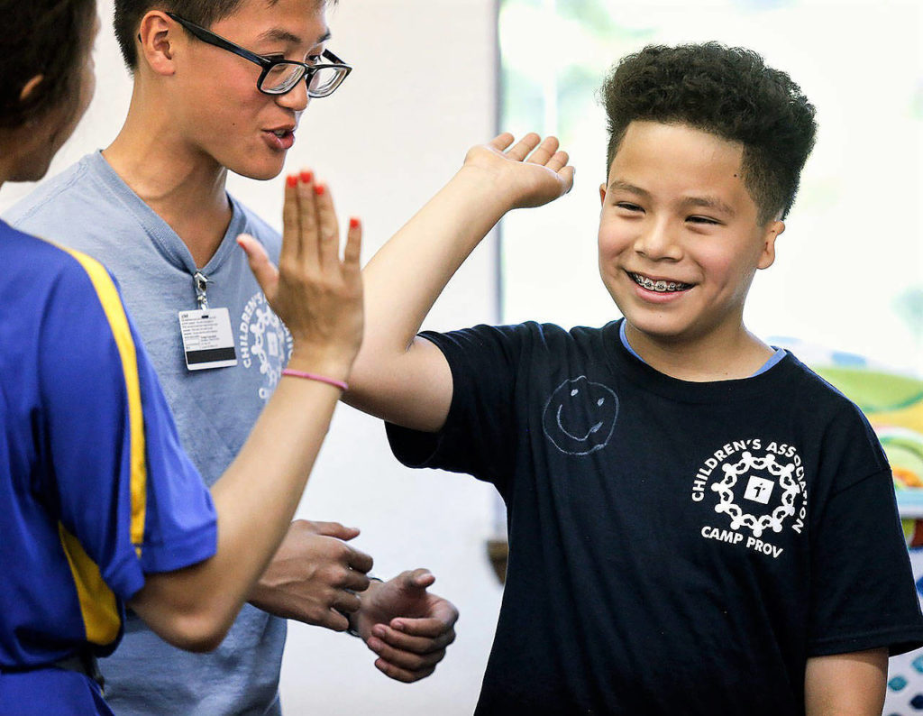 Anthony Vu, a teen volunteer at Camp Prov, looks on as a camper high-fives a unit leader at Forest Park in 2019. (Dan Bates / Herald file)
