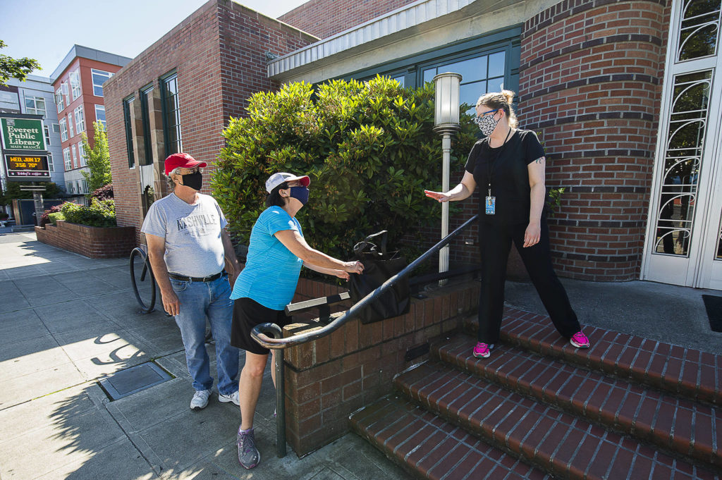 Leslie Bringedahl grabs a bag containing books she and her husband Mark ordered June 17 after Everett Public Library Circulation Manager Carol puts them down on a wall for curbside pickup at the Everett Public Library main branch in Everett. (Andy Bronson / Herald file)
