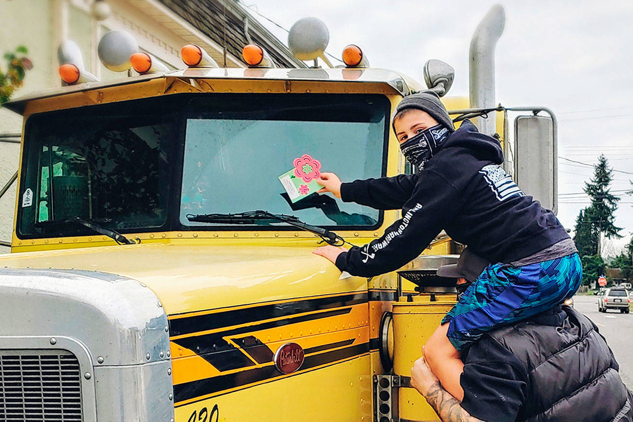 Eagle Creek Elementary fourth grader, Cameron Lowber, sits on his dad Caleb’s shoulders as he places a kindness message on a semi-truck in downtown Arlington. (Arlington Public Schools)