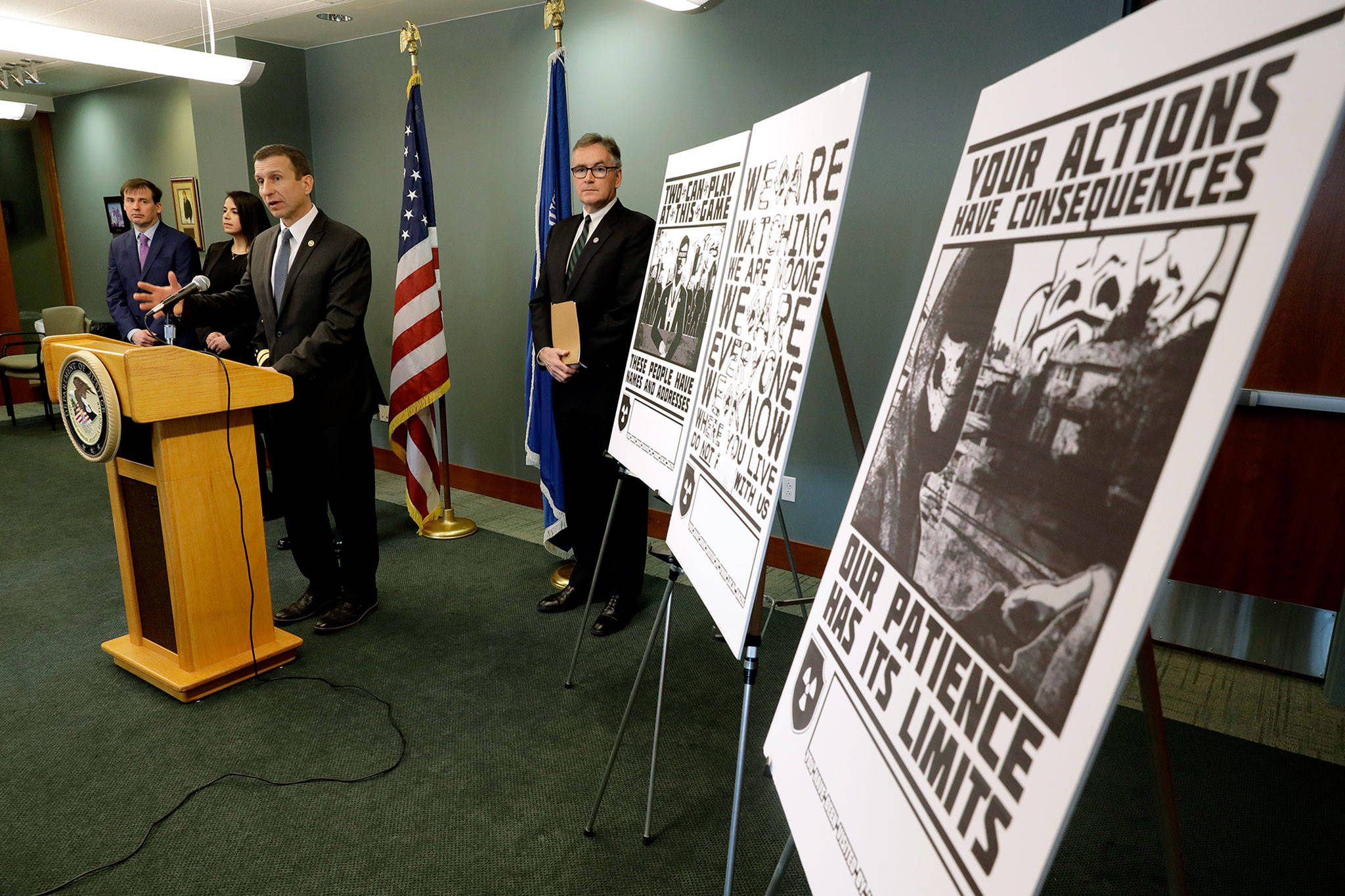 Raymond Duda (at podium), FBI Special Agent in Charge in Seattle, speaks during a news conference Feb. 26 about charges against a group of alleged members of the neo-Nazi group Atomwaffen Division for cyber-stalking and mailing threatening communications — including the Swastika-laden posters at right — in a campaign against journalists in several cities. (AP Photo/Ted S. Warren, file)
