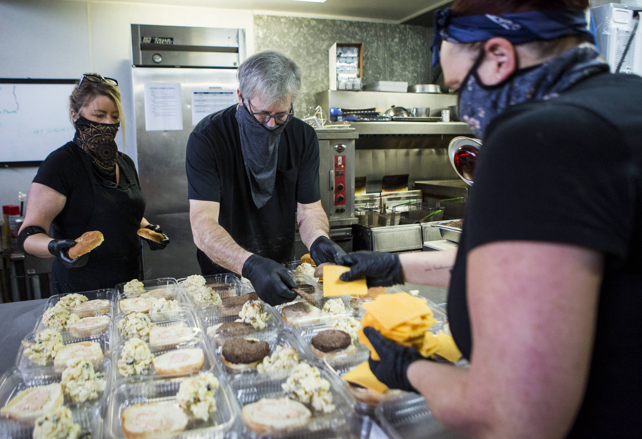 Jennifer Carlson, left to right, Jim Staniford and Katherine Stipech put together cheeseburger and potato salad meals Thursday for the Everett Gospel Mission in Everett. (Olivia Vanni / The Herald)