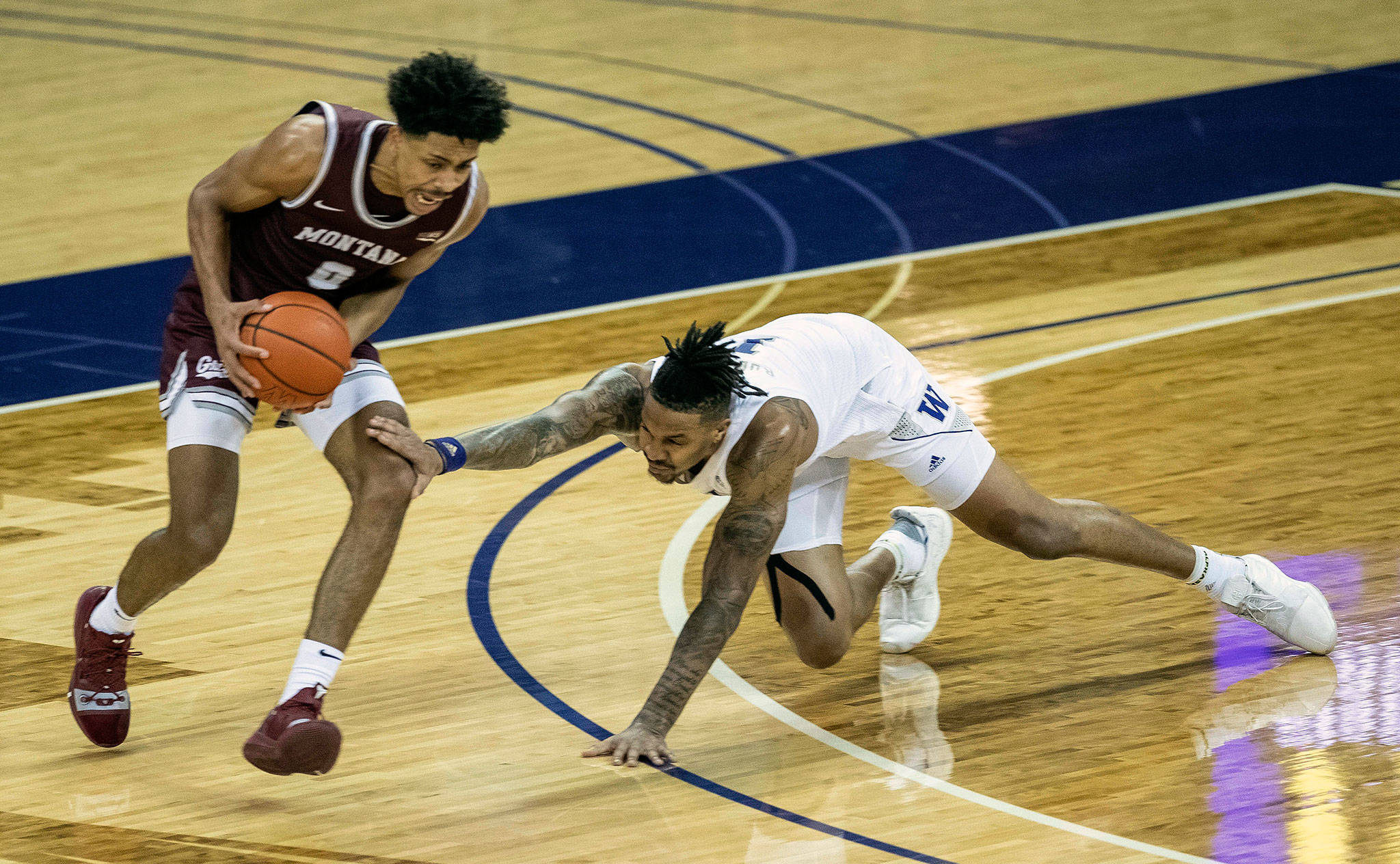 Washington’s Nate Roberts (right) stumbles while defending Montana’s Kyle Owens in the first half of a game on Dec. 16, 2020, at Alaska Airlines Arena in Seattle. (Dean Rutz/The Seattle Times via AP)