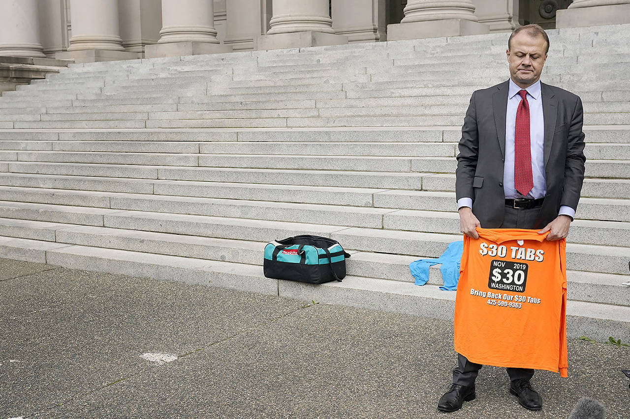 Tim Eyman holds a T-shirt from his long-running campaign for $30 car tabs Oct. 15 at the Capitol in Olympia. (AP Photo/Ted S. Warren, file)