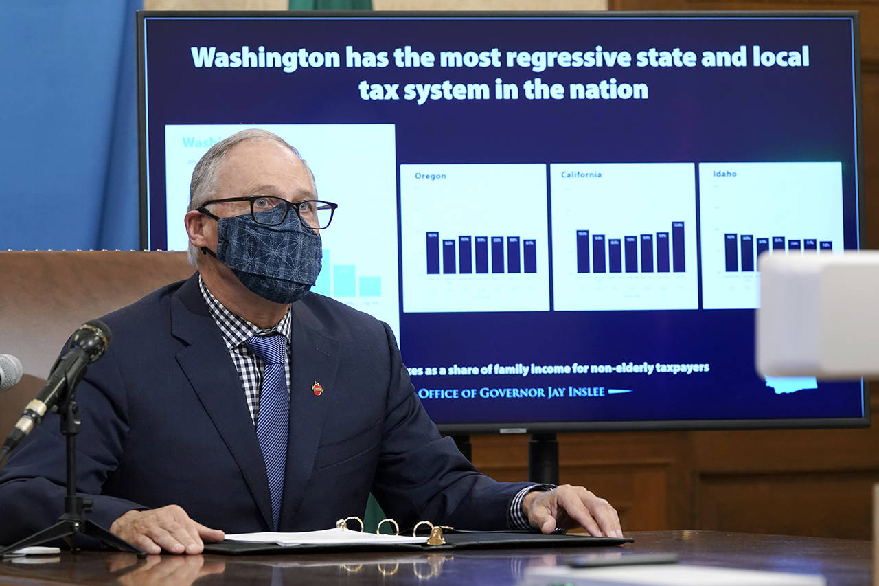 Washington Gov. Jay Inslee sits in front of a chart comparing Washington state’s tax system to other western states as he talks to reporters Thursday at the Capitol in Olympia, Wash. (AP Photo/Ted S. Warren)