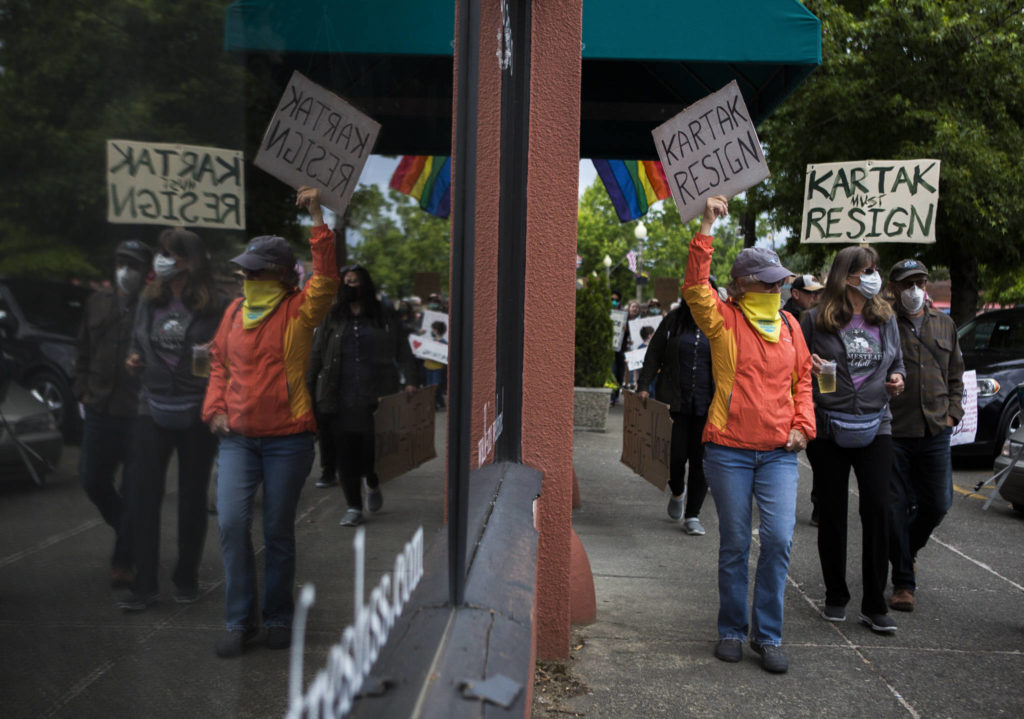 A group of protesters holding signs calling for Snohomish Mayor John Kartak’s resignation walk down First Street on June 5 in Snohomish. (Olivia Vanni / The Herald)
