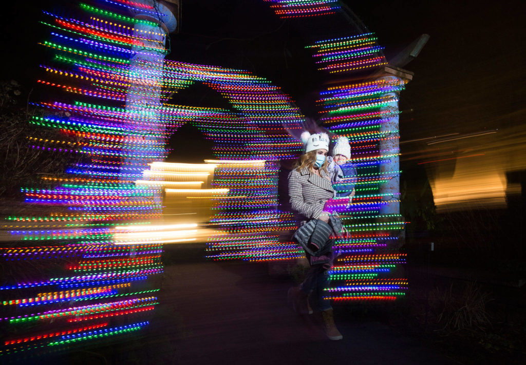 Chelsie Assink and her daughter, Paisley, of Bellingham, walk through lights at the front entrance of the Wintertide Lights at Evergreen Arboretum in Legion Park in Everett. For the first time, the Evergreen Arboretum is lit up for the holidays. Wintertide Lights will be up through New Year’s Eve and are open from dusk to 8 p.m. (Andy Bronson / The Herald)
