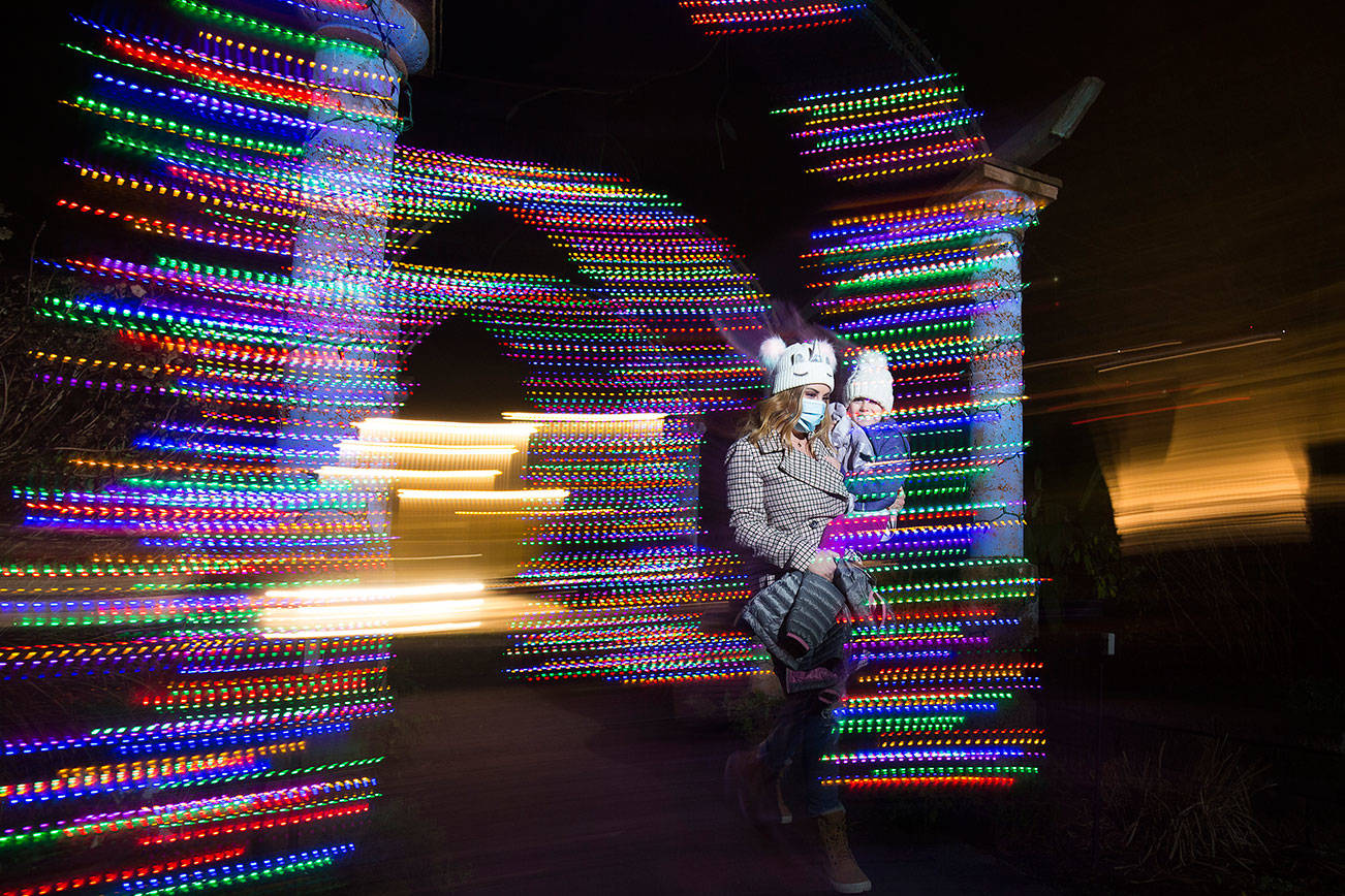 Chelsie Assink and her daughter Paisley, of Bellingham, walk through lights at the front entrance to look at the Wintertide Lights at Evergreen Arboretum in Legion Park on Tuesday, Dec. 22, 2020 in Everett, Washington. For the first time, the Evergreen Arboretum is lit up for the holidays. The Wintertide Lights will be up through New Year's Eve and open from dusk to 8 p.m.  (Andy Bronson / The Herald)