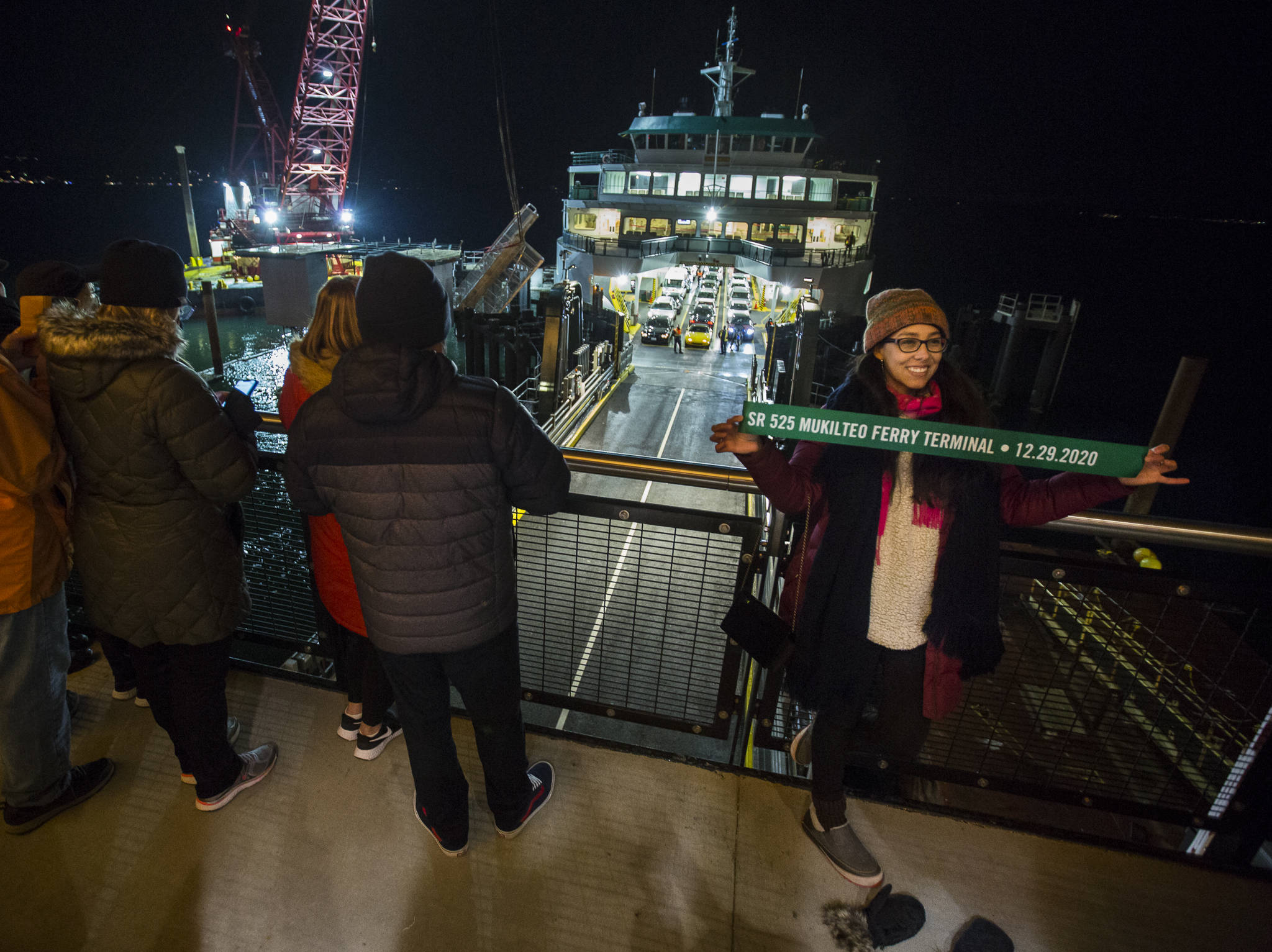Sofia Samoyoa takes a photograph with a commemorative ribbon as the first car passengers to use the new Mukilteo ferry terminal off-load on Tuesday. (Olivia Vanni / The Herald)