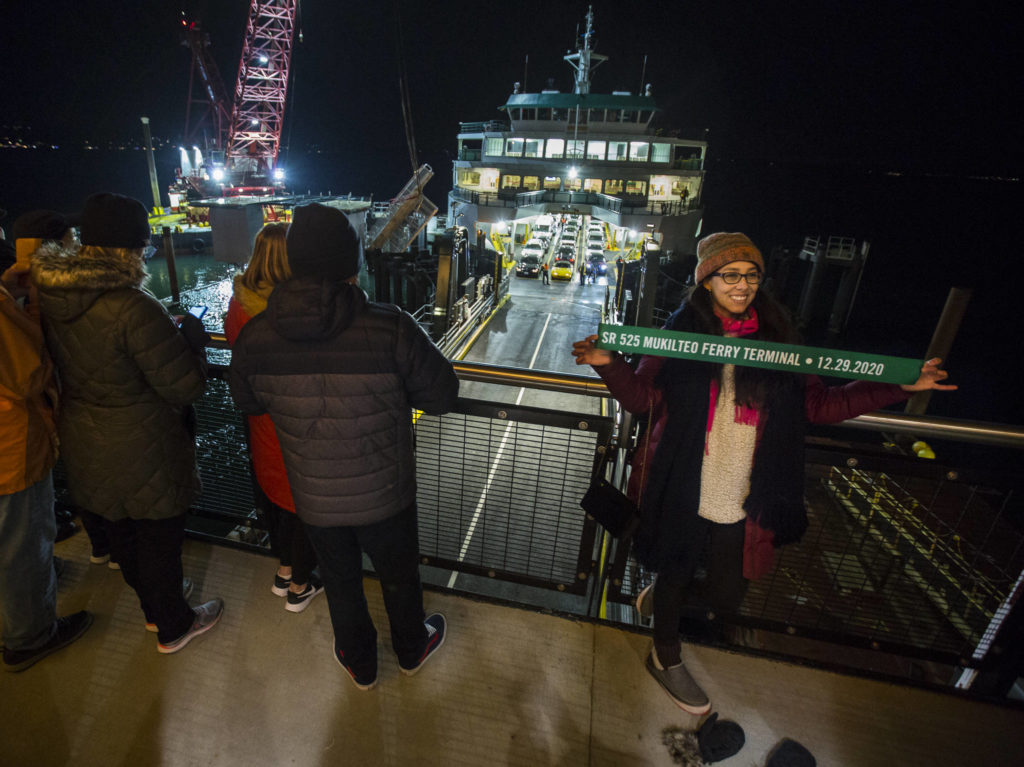 Sofia Samoyoa takes a photograph with a commemorative ribbon as the first car passengers to use the new Mukilteo ferry terminal off-load on Tuesday. (Olivia Vanni / The Herald)
