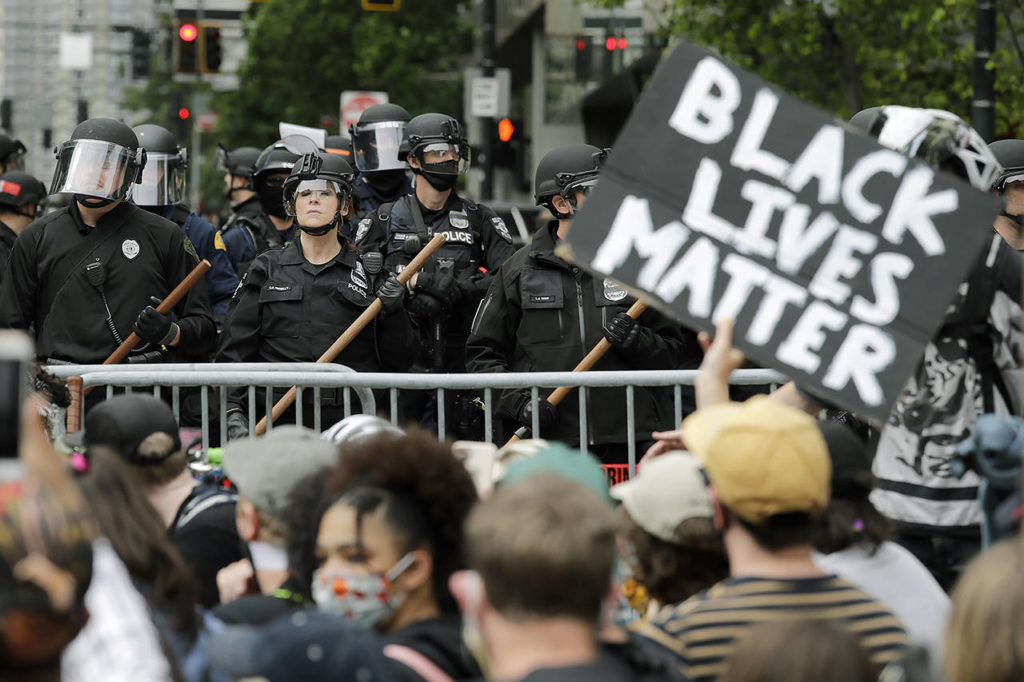 In this June 3 photo, police officers behind a barricade look on as protesters fill the street in front of Seattle City Hall in Seattle, following protests over the death of George Floyd, a Black man who was in police custody in Minneapolis. Protests in Seattle over the killing of Floyd were among Washington state’s top stories for 2020. (AP Photo/Elaine Thompson, File)
