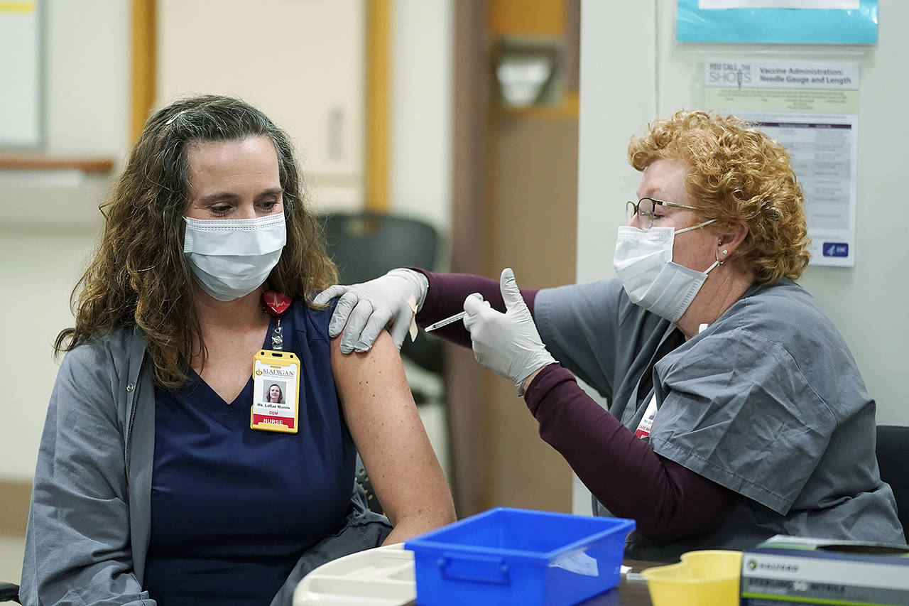LaRae Munns (left), a nurse in the Emergency Department at Madigan Army Medical Center, receives one of the first doses of the Pfizer vaccine for COVID-19 from nurse Goldie Martin on Dec. 16 at Madigan Army Medical Center at Joint Base Lewis-McChord. (AP Photo/Ted S. Warren, file)