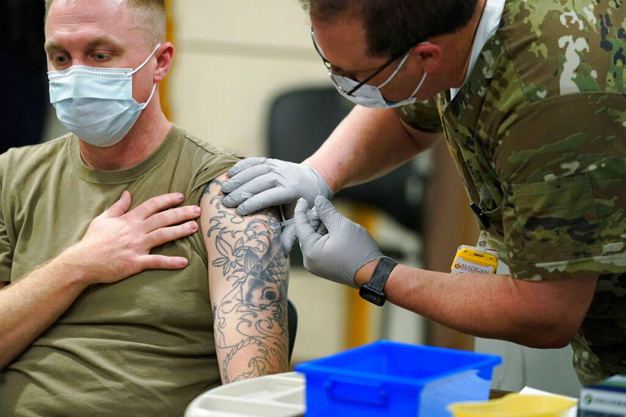 Staff Sgt. Travis Snyder (left) receives the first dose of the Pfizer vaccine for covid-19 given at Madigan Army Medical Center at Joint Base Lewis-McChord, Dec. 16, in Washington state. Nurse Jose Picart administered the shot. Vaccinations are scheduled to continue in the coming weeks for front-line medical workers and and others in high-priority positions at the base. (Ted S. Warren / Associated Press)