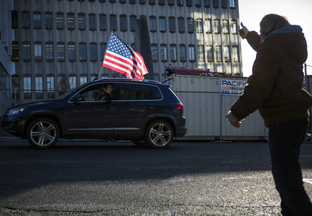 A Trump supporter waves as a man gives him a thumbs up as the Trump rally caravan drives by the Snohomish County Courthouse on Wednesday, Jan. 6, 2020 in Everett, Wa. (Olivia Vanni / The Herald)
