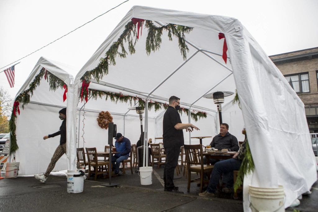 The Oxford Saloon owner Craig Swanson takes the orders from customers dining outdoors along First Street in Snohomish last month. Gov. Jay Inslee on Tuesday announced that some COVID-19 restrictions would be eased as soon as next week. (Olivia Vanni / Herald file)
