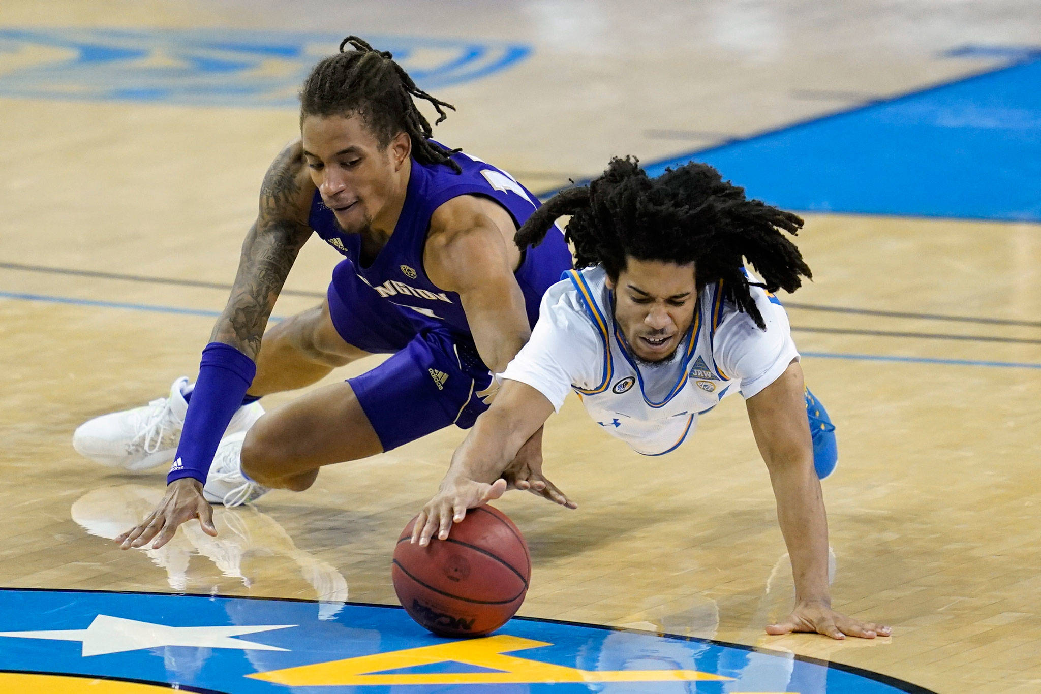 Washington forward Hameir Wright (left) and UCLA guard Tyger Campbell dive for a loose ball during the second half of a game Jan. 16, 2021, in Los Angeles. (AP Photo/Ashley Landis)